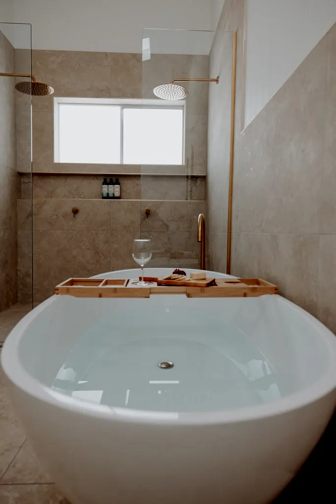 Freestanding bath inside a tiled bathroom with rainfall shower and timber bath tray.