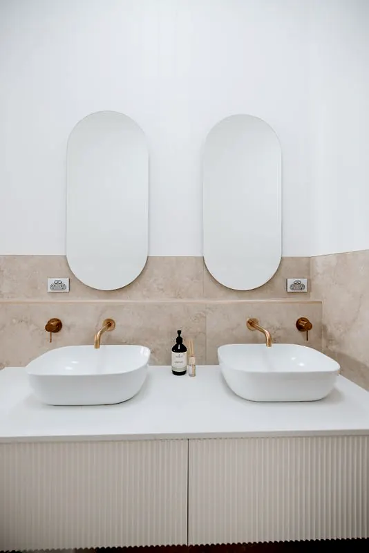 Bathroom with double vanity, stone finishes, and brushed brass fixtures.