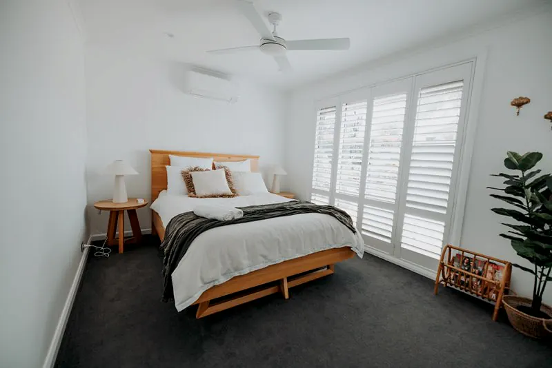 Bright bedroom with timber bed frame, plantation shutters, and clean styling.