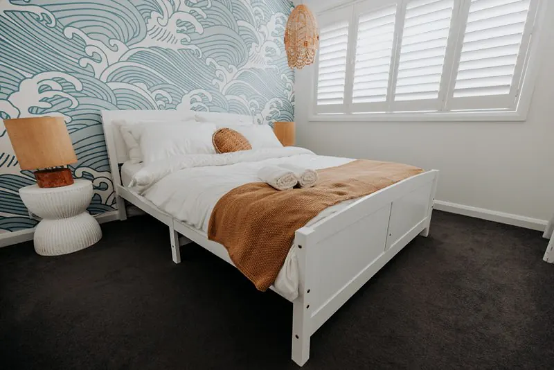 Bedroom with a statement wave-pattern wall, white bed frame, and warm natural styling.