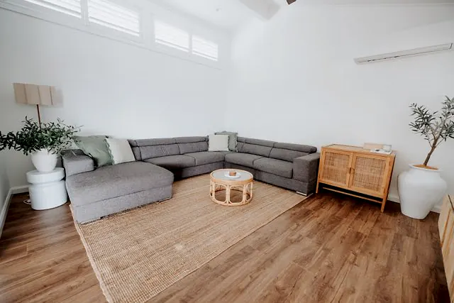 Light-filled living room with sectional sofa, timber floors, and woven rug.
