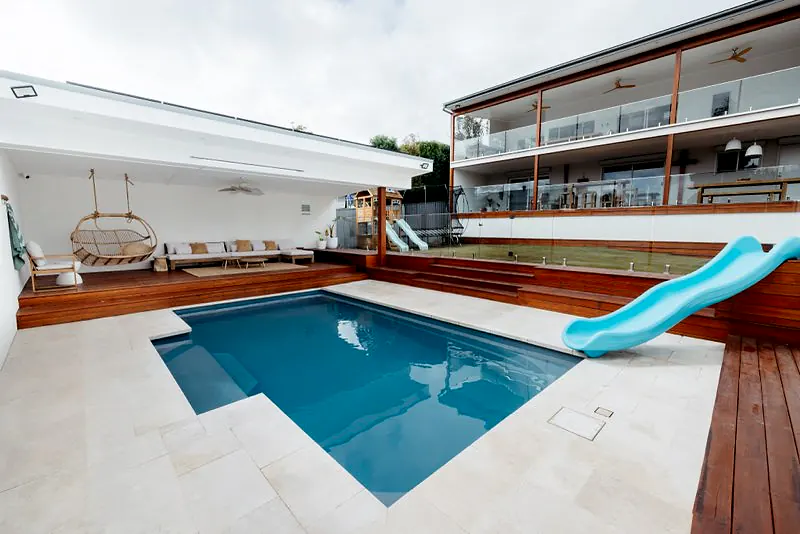 Modern pool area with timber decking, slide, and large entertaining spaces.